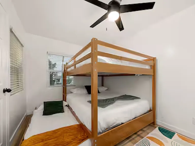 Bedroom with a queen-over-queen bunk bed and a twin trundle, sleeping up to 5 people. Includes a dedicated desk/vanity area and direct access to the sunroom for a seamless connection to the outdoor space.