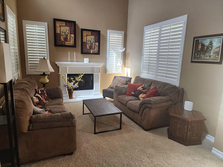 Comfortable living room with a central fireplace, ample seating, and plantation shutters for light and privacy.