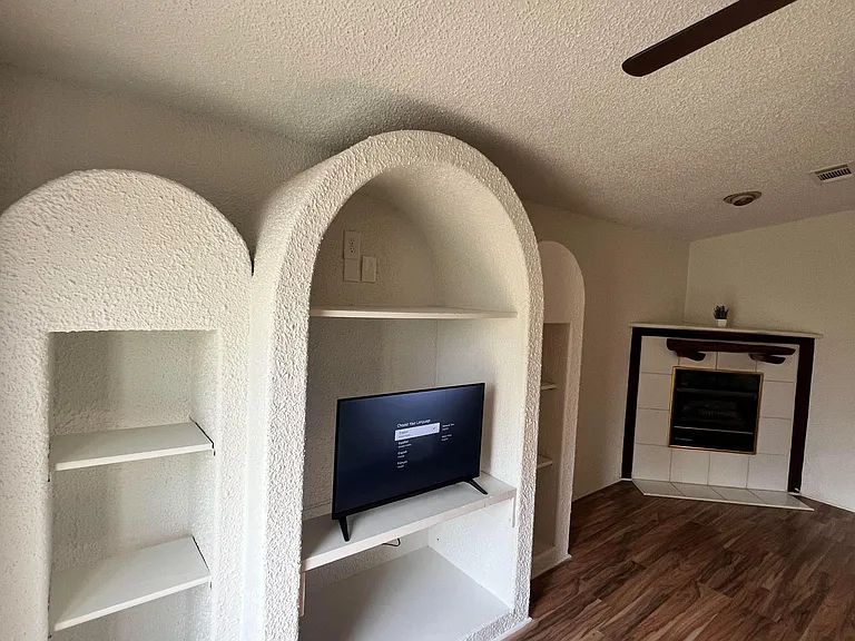 Open living area with built-in arched shelving, durable wood-look flooring, and a tiled fireplace for added character.