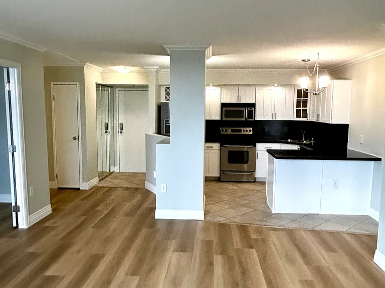 View from living area to kitchen, front entrance and second bedroom on left