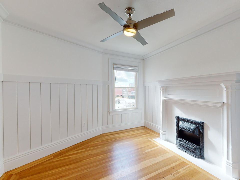 Bright room with hardwood floors, paneled walls, a window, and a decorative fireplace, modern ceiling fan above