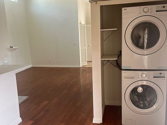 View from dining nook out to main living space, showing in-unit washer/dryer with new shelving and vaulted ceilings in living space.