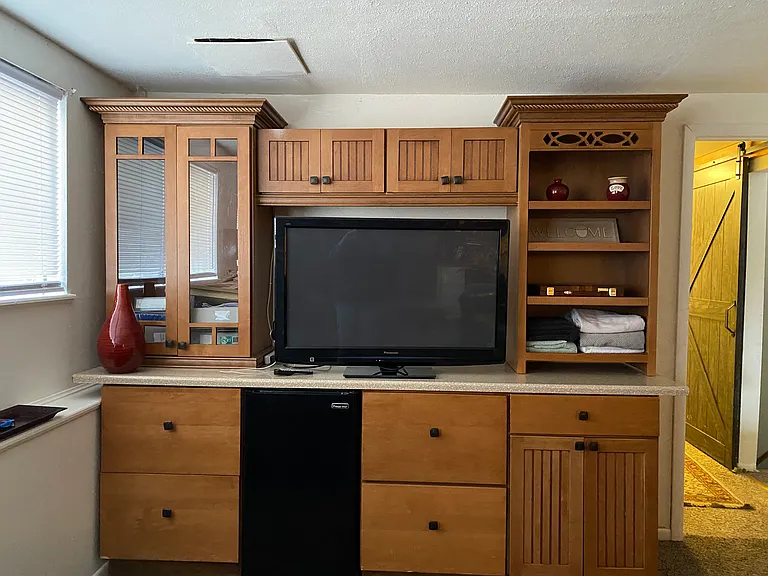 "Fireplace Suite" with mini fridge, big screen TV, huge windows (on left), sliding "barn door" style hallway door, private wing with bathroom next door. Fireplace, couch, "man cave" style room with two stacking bunks (3 twins each) on right.
