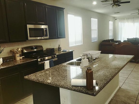 Open-concept kitchen with granite island, double sink, and stainless appliances, flowing into a spacious living area.