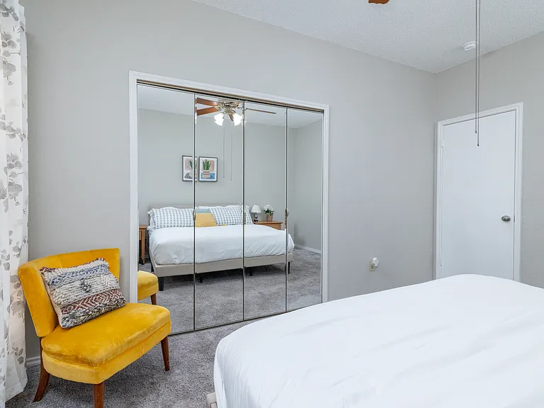 Primary bedroom on the first floor features a king bed, cozy chair, mirrored closet doors, and a ceiling fan for added comfort.