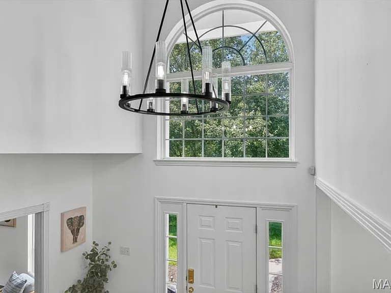 Two-story foyer featuring an arched transom window, a white paneled front door with sidelights, a contemporary circular chandelier, and white wall trim details