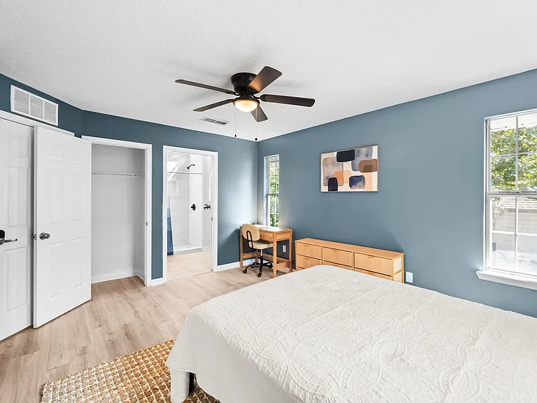 Spacious bedroom with a ceiling fan, large windows, and an open closet plus a dedicated desk nook for work or study.