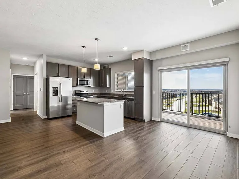 Floor-to-ceiling natural light and an airy open layout bring the kitchen, living area, and private balcony together in one beautifully connected space.
