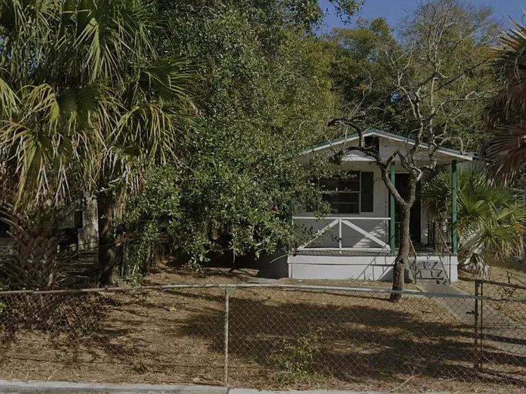 Single-story home with a covered front porch, mature trees, and a fenced front yard for added privacy.