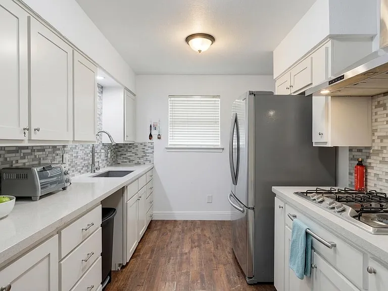 Galley kitchen with ample white cabinetry, long counters, mosaic tile backsplash, and stainless appliances for easy meal prep