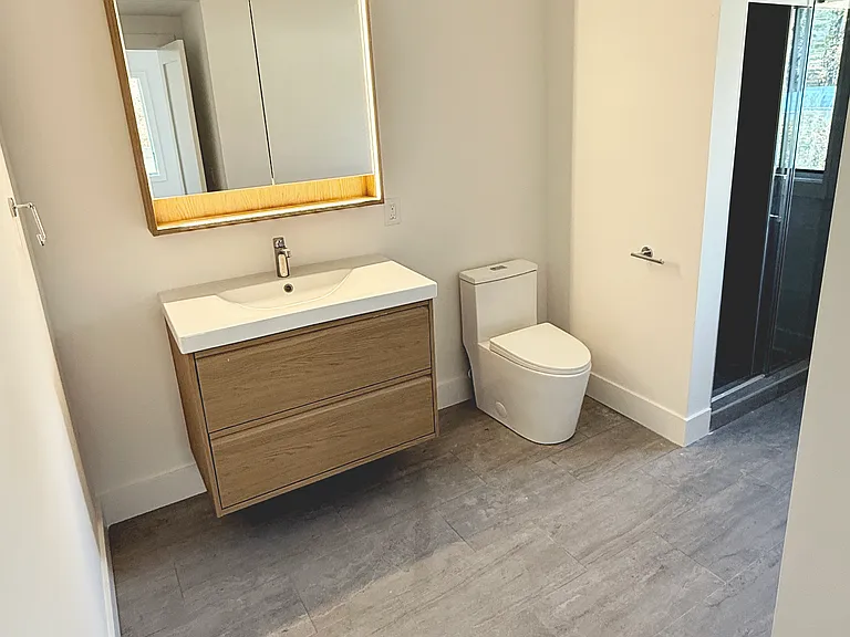 Bathroom with contemporary toilet, shower with sliding glass door and oak vanity