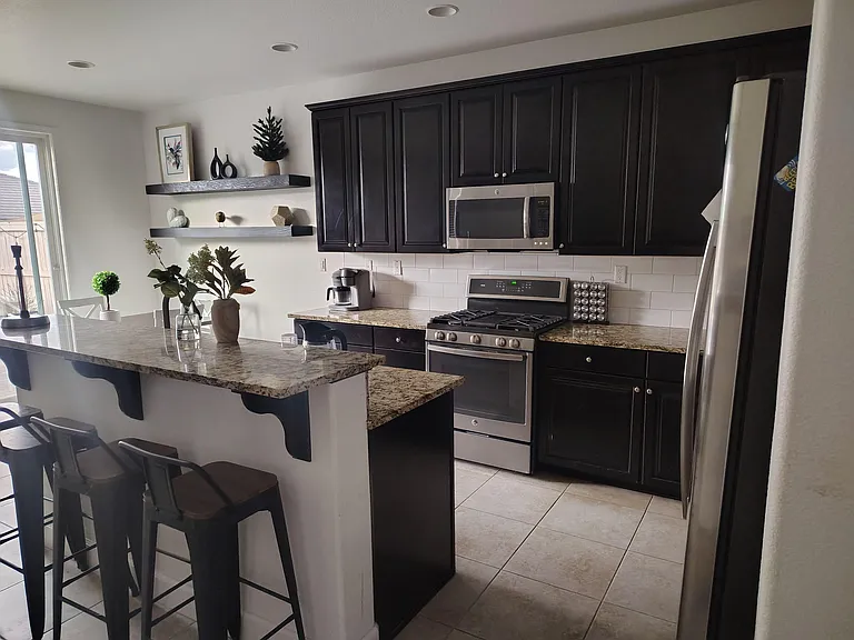 Spacious kitchen with granite breakfast bar seating, stainless appliances, ample cabinetry, and open shelving for storage.