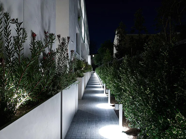 Illuminated Garden-Level Walkway at Night _ A serene pathway lined with lush greenery and soft lighting, guiding residents through the beautifully landscaped exterior spaces.