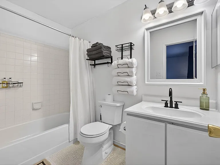 Clean full bath with tub/shower combo, tile surround, vanity sink, and wall shelving for towel storage.