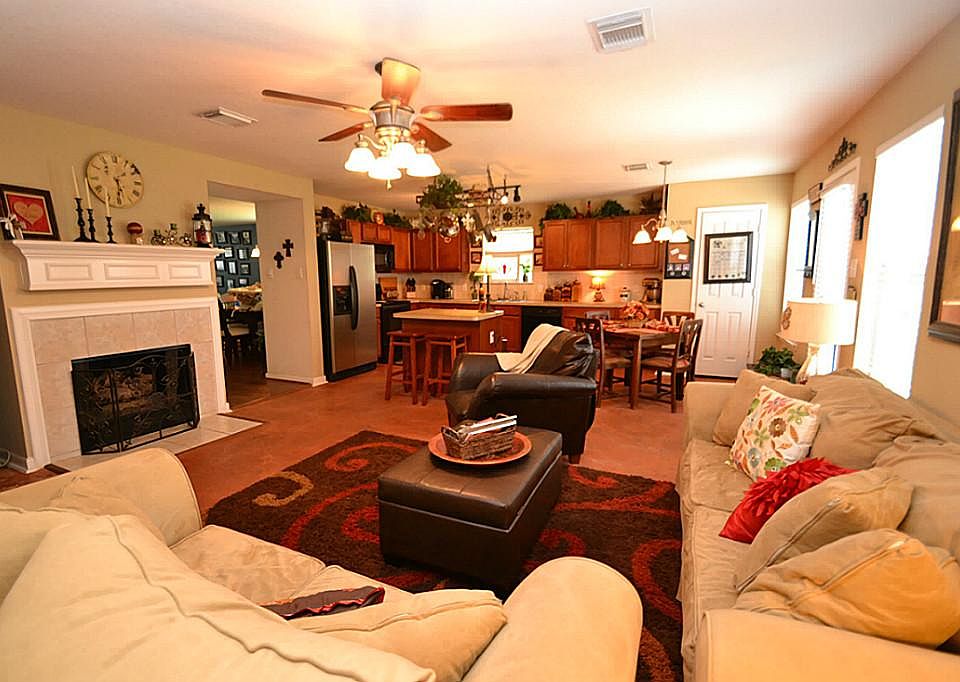 Family room featuring stained concrete floors, ceiling fan with light fixture, fireplace with gas logs and open to the kitchen and breakfast room.