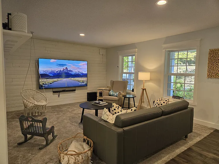Living room featuring a couch, armchair, swinging chair, and an 85" TV