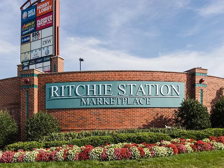 Monument sign at Ritchie Station Marketplace with landscaped flowerbeds, indicating nearby retail and dining options.