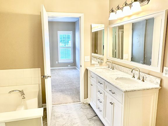 Bright master bathroom with marble floors, dual sinks, spacious vanity, large garden bathtub, and walk-in shower.