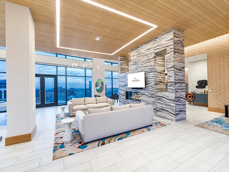Resident lounge with city views, sculptural lighting, and tailored seating centered around a fireplace for connection, conversation, and relaxed downtime.