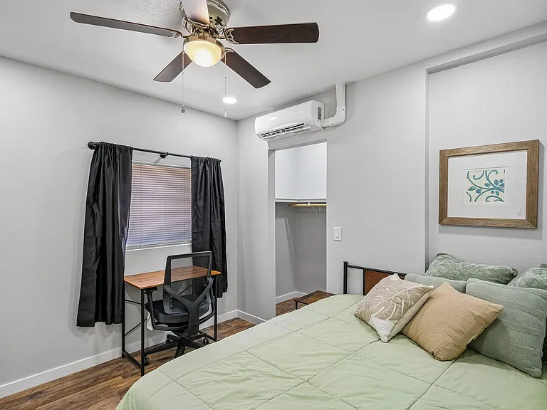Furnished bedroom with a full sized bed, desk area, ceiling fan, mini-split A/C and large open closet storage.