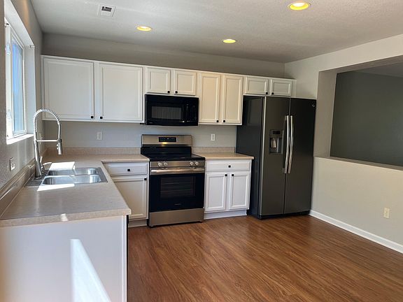 Newly refreshed white kitchen with laminate flooring, brand new range, and new kitchen faucet.