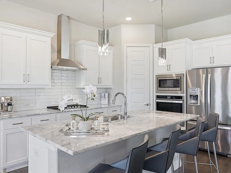 White shaker cabinetry with crown molding, stainless steel appliances, and a quartz island with seating.