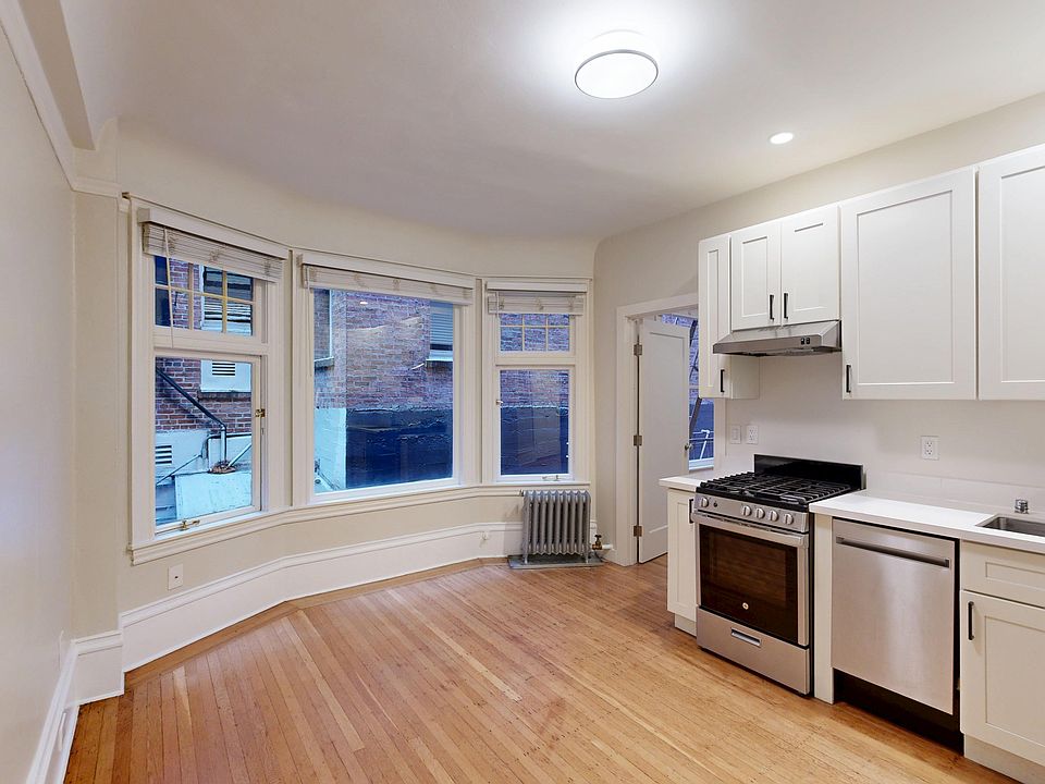 Bright kitchen featuring cabinets, stainless steel appliances, hardwood floors, and large windows with city views