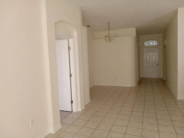 View from the living room area up to the front doorway. The laundry room entrance is to the left of the front door. The dining area is under the light fixture. The Master bedroom is the closest doorway to the left. The kitchen area is to the right.