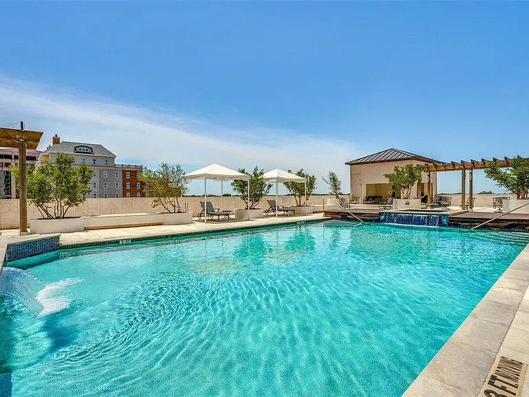 Outdoor swimming pool featuring a waterfall edge, surrounding stone coping, a shaded cabana, and a pergola structure