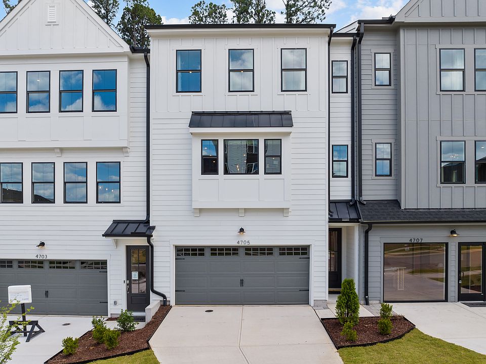 A modern, multi-story townhouse with a gray exterior, large windows, and a garage door in the foregr