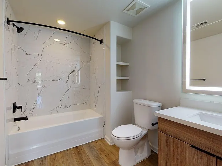 Apartment bathroom with large soaking tub, LED vanity mirror, and wood style floor.