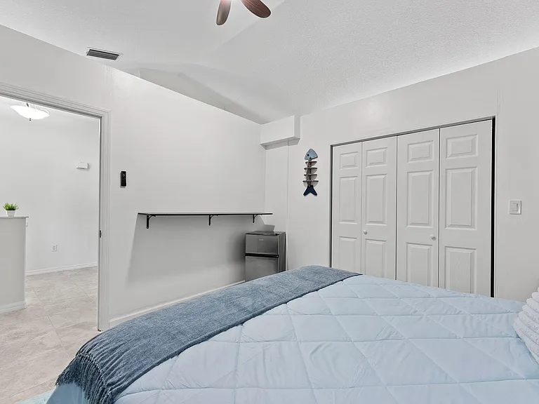 Bedroom with double-door closet, wall-mounted shelf/desk space, ceiling fan, and convenient mini fridge.