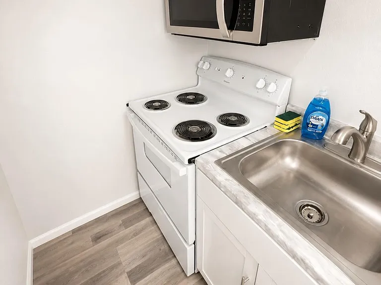 Compact kitchen nook with electric range, over-the-range microwave, stainless sink, and ample base cabinetry.