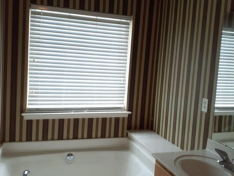 Full bath with a soaking tub/shower combo, single-sink vanity, and a window with blinds for natural light.