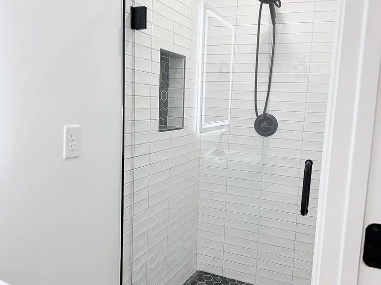 Walk-in tiled shower with built-in niche shelving, matte-black fixtures, and a glass enclosure for easy upkeep.