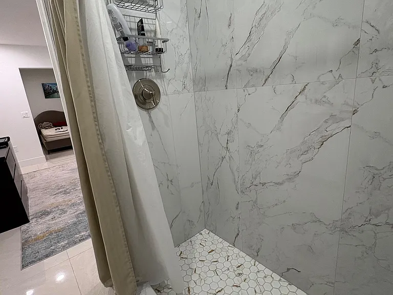 Walk-in shower with large-format marble-look tile, hex mosaic floor, and built-in shower caddy for easy storage.