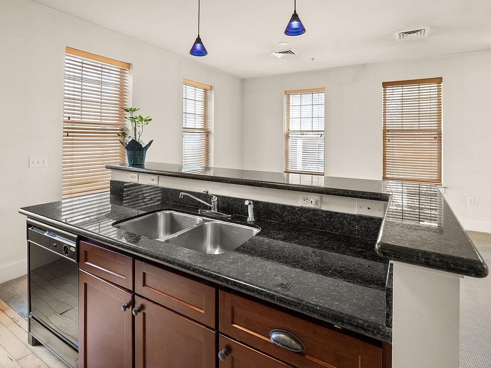 Double-bowl stainless kitchen sink with four-stool counter and granite countertops. Living/dining area in background.