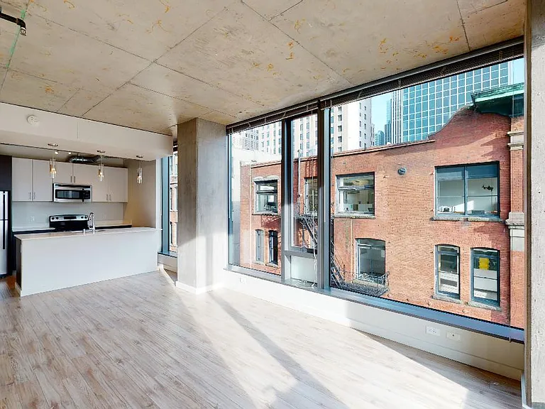 Apartment kitchen with stainless steel appliances, dining and living room with wood-style flooring and floor-to-ceiling windows.