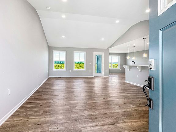 Unfurnished great room with vaulted ceiling, large windows, and wood-like flooring. Open floor plan