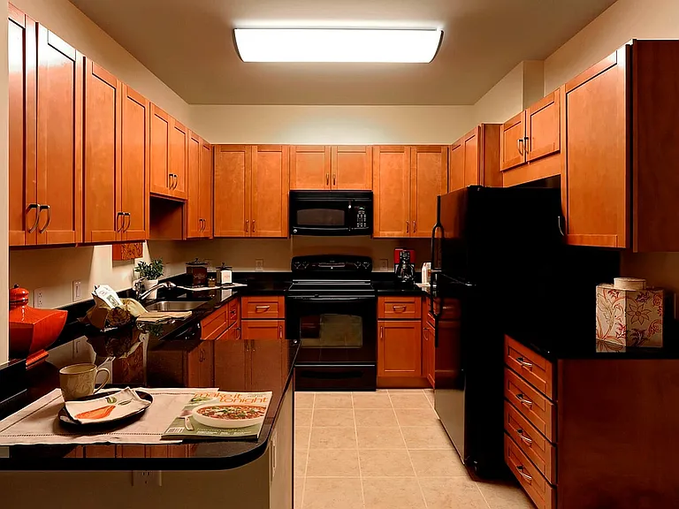 Warm & Inviting Kitchen With Wooden Cabinetry, Black Appliances, & Granite Countertops