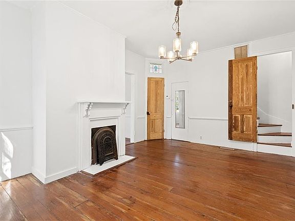 Unfurnished living room with visible vents, stairway, wood finished floors, a fireplace, and a notable chandelier