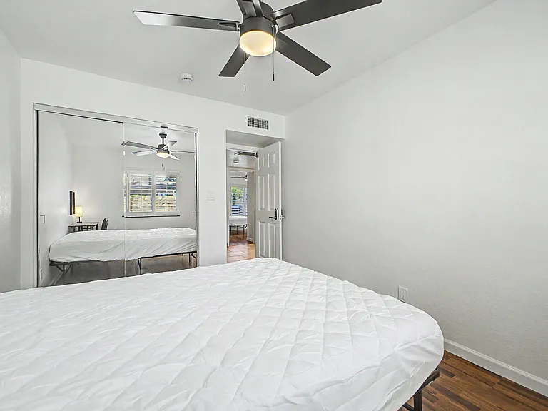 Wood flooring, Queen Bed, desk, chair, lamp, fan, mirrored closet.