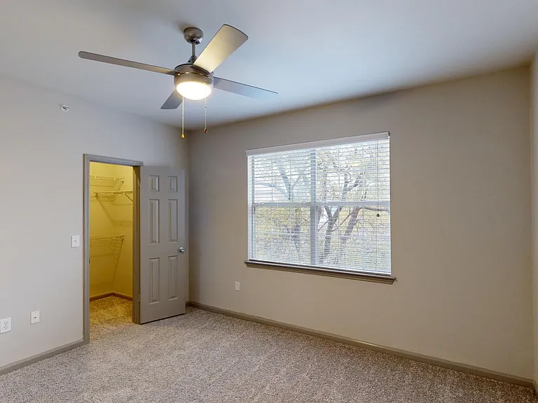 Spacious apartment bedroom with large closet and plush carpet flooring.