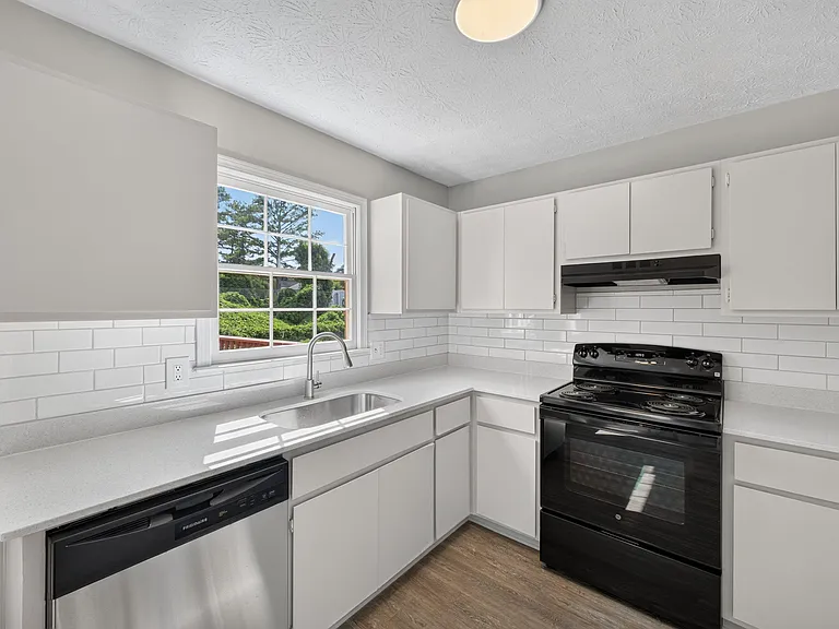 Efficient U-shaped kitchen with ample cabinet storage, subway-tile backsplash, and a full appliance set plus window over sink
