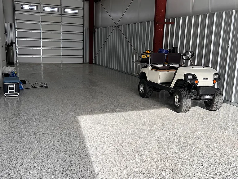 Clean oversized attached shop/garage with epoxy-style flooring, tall roll-up door, and room for boat, golf cart, trailer, tools, or extra storage.