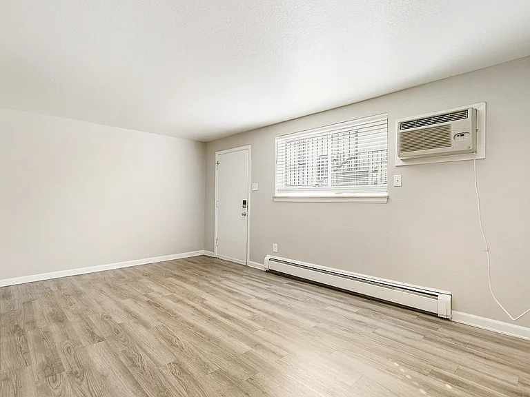 Bright room with sleek wooden floors, modern air conditioning unit, and ample natural light providing a warm and inviting atmosphere.