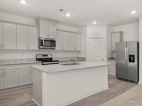The kitchen has stainless steel appliances and plank flooring.