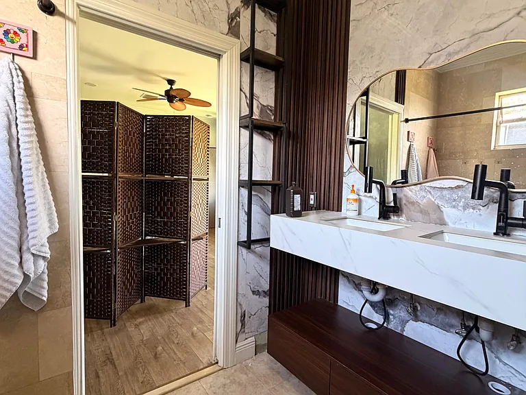 Updated bathroom with a double-sink vanity, marble-look finishes, open shelving, and a large mirror for easy routines.
