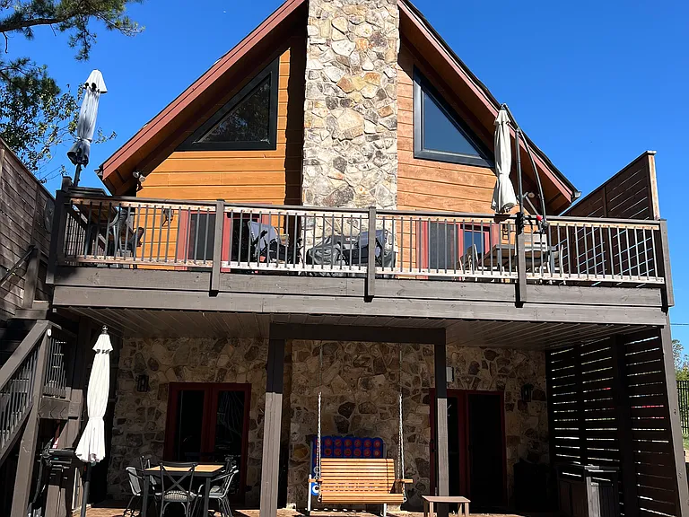 Backside of the house with lake views. Upper deck and lower covered cement patio. Each area includes outdoor dining table, chairs and shade umbrellas.