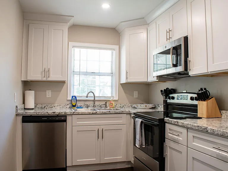 Updated kitchen with shaker cabinets, granite-look counters, dishwasher, range with microwave, and a window over the sink.